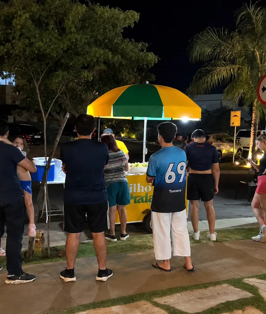 Público reunido em volta do carrinho Milho da Praia durante evento à noite